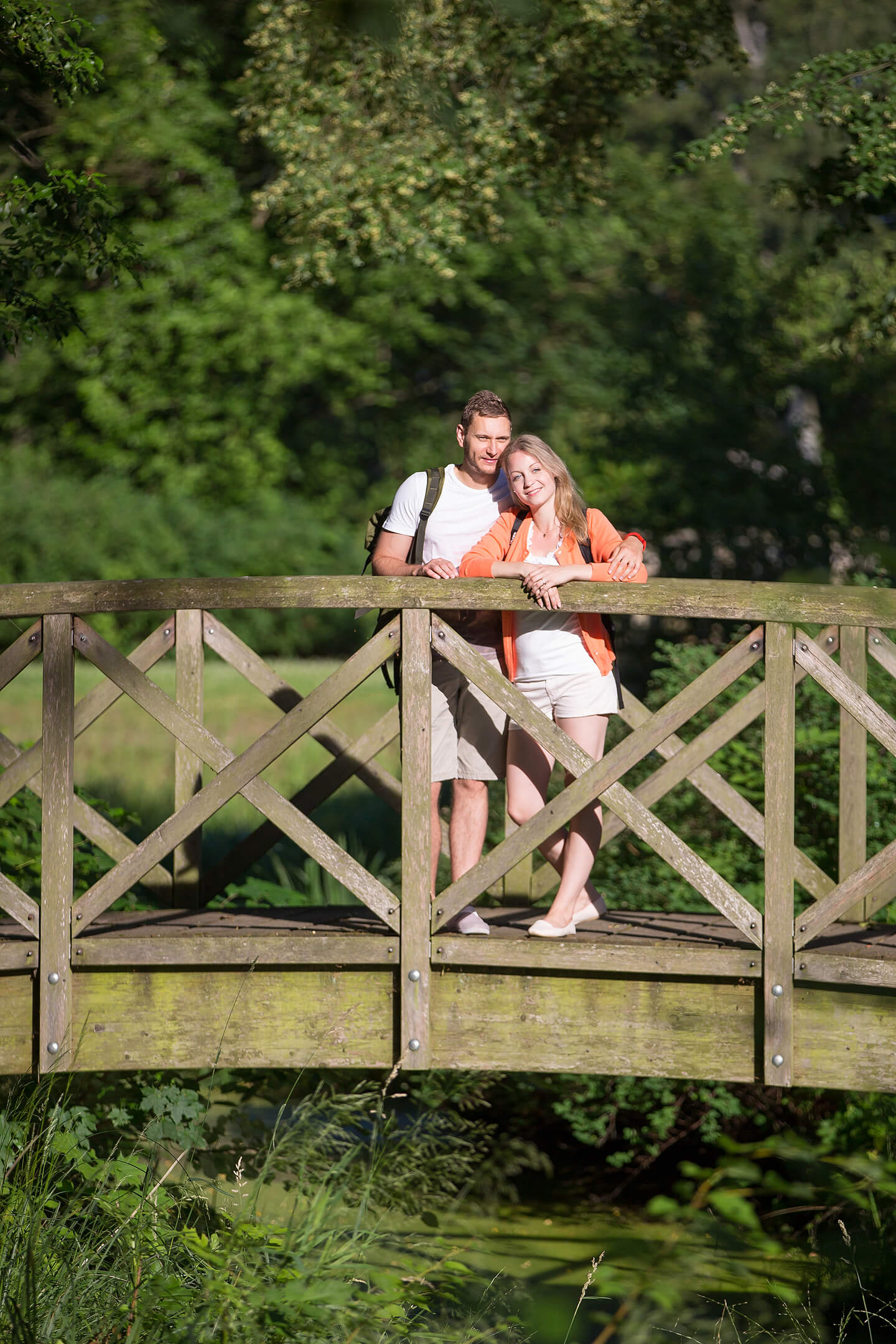 Pärchen auf Holzbrücke blickt in die Ferne und wird vom Sonnenlicht beschienen