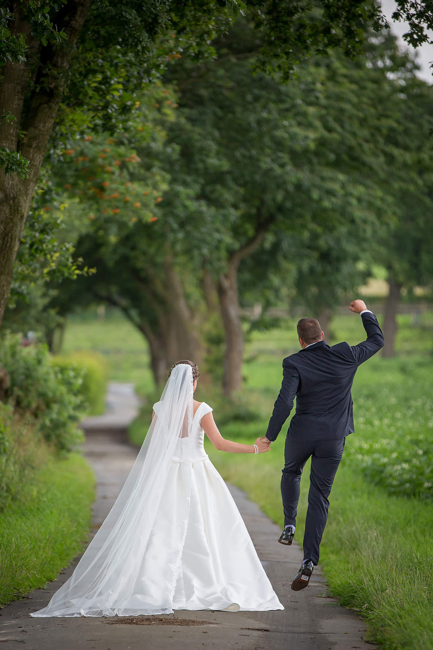 Brautpaar von hinten fotografiert und der Bräutigam springt vor Freude in die Luft
