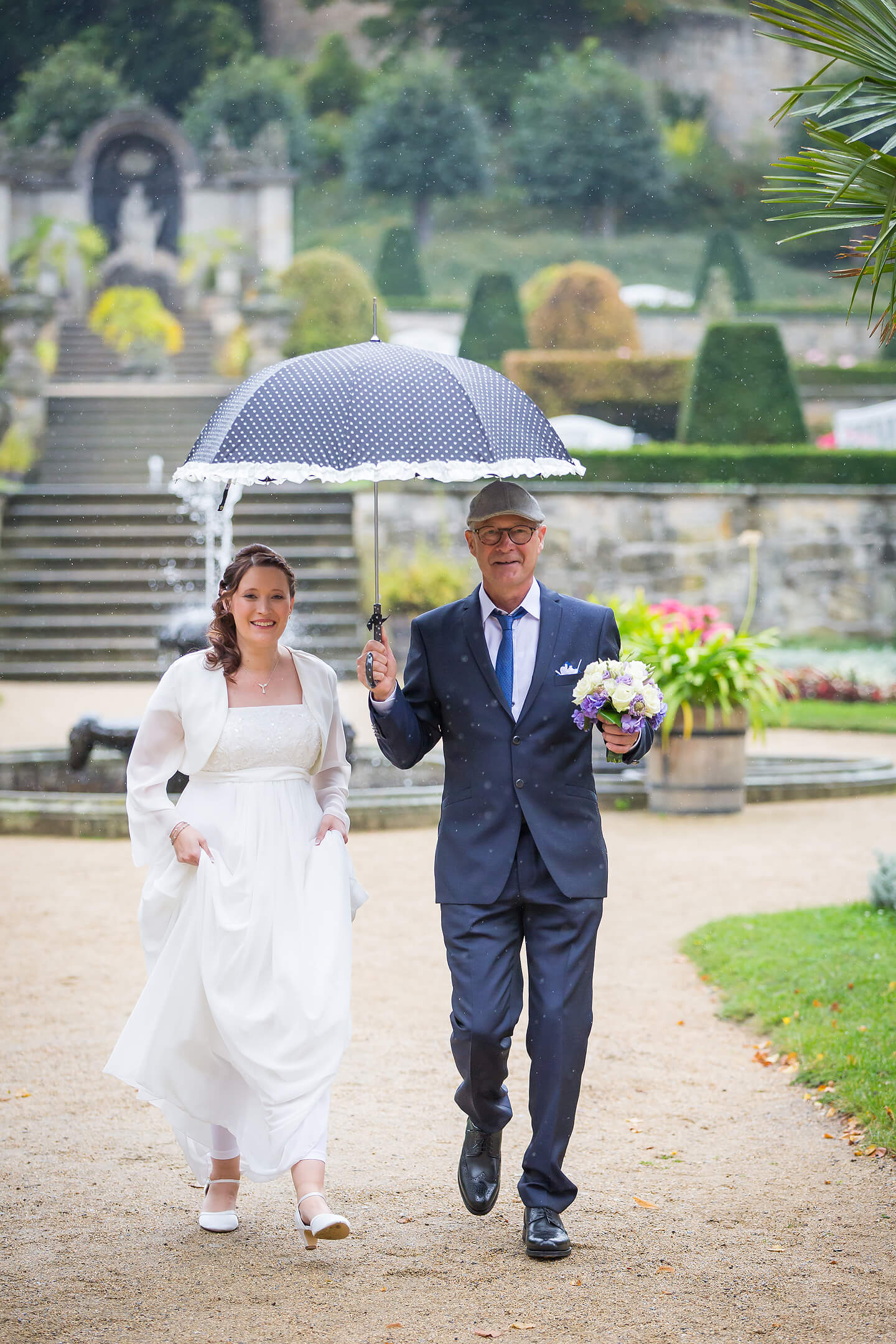 Vater führt die Braut im Schlosspark zur Trauungszeremonie