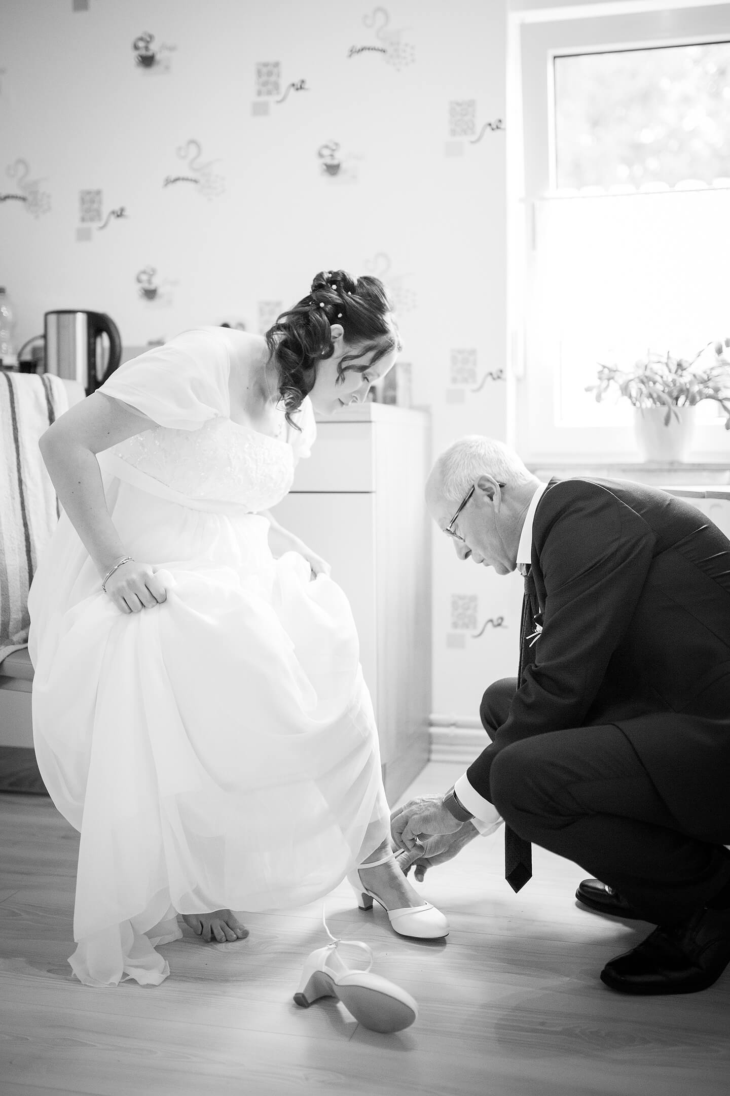 Vater zieht seiner Tochter die Brautschuhe an