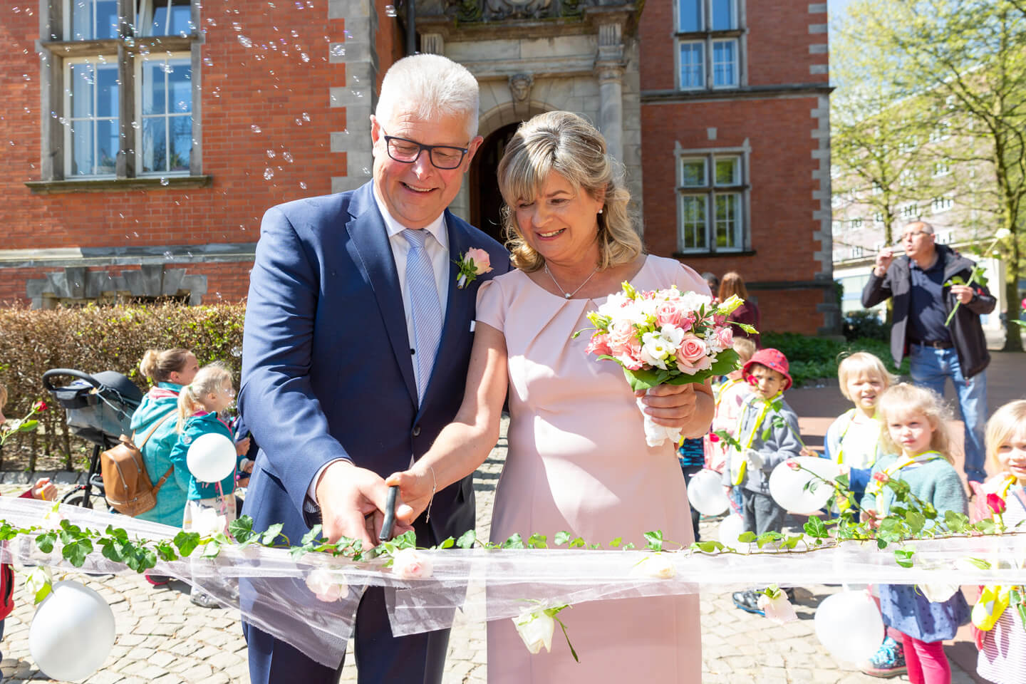 Hochzeitspaar zerschneidet vor dem Standesamt einen Schleier