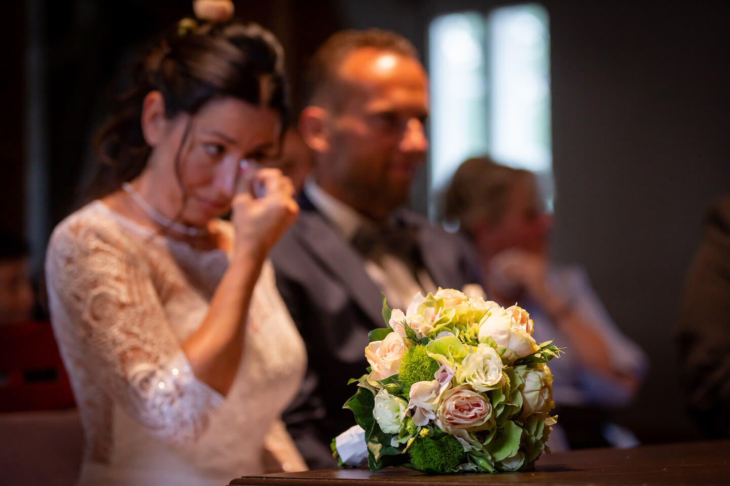 Brautstrauss - im Hintergrund ist verschwommen das Brautpaar zu erkennen