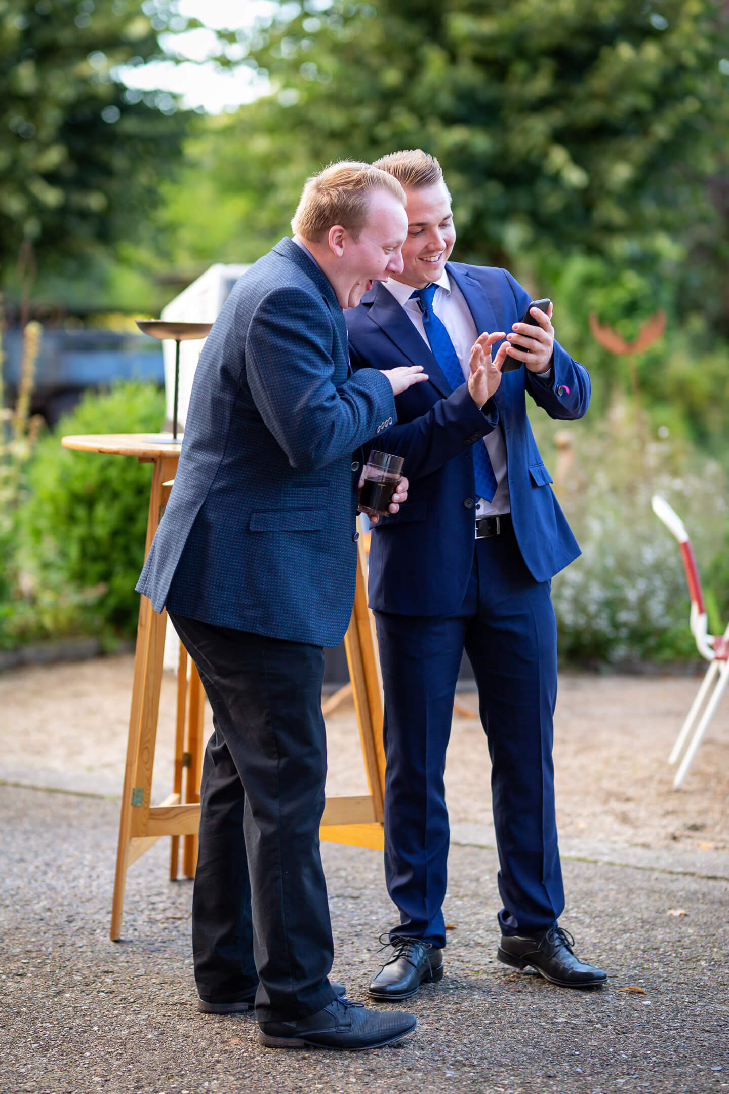 Zwei Gäste schauen lachend auf ein Handy während einer rauchpause vor der Tür der Hochzeitslocation