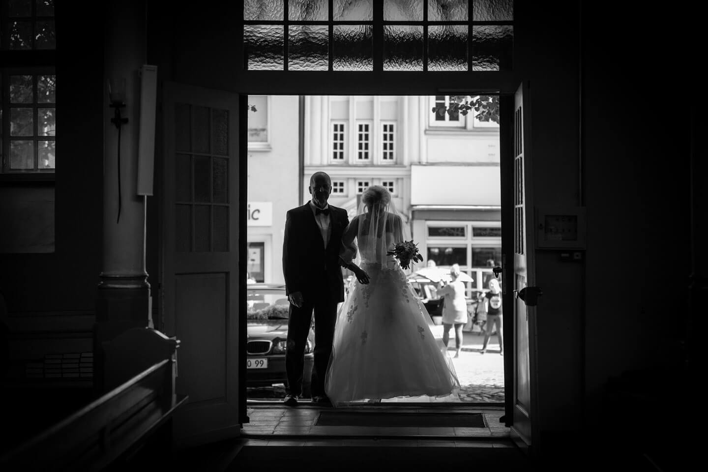 Braut mit Brautvater im Eingangsbereich der Kirche im Gegenlicht