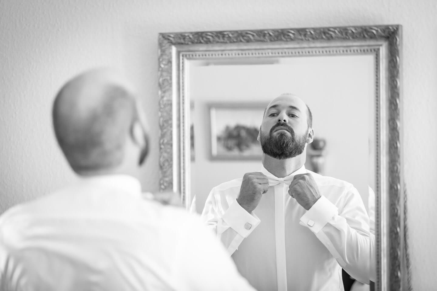 Bräutigam zupft sich die Fliege vor dem Spiegel zurecht