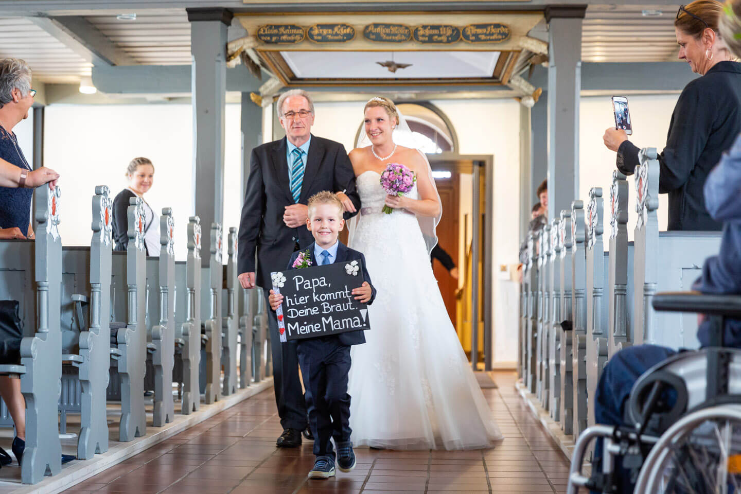 Braut wird vom Vater zum Altar geführt, Kind geht vorweg