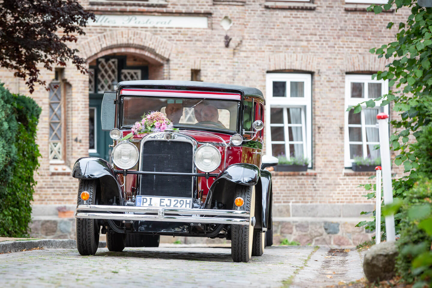 Hochzeitsauto faehrt durch kleine Gasse neben der Kirche in Barmstedt