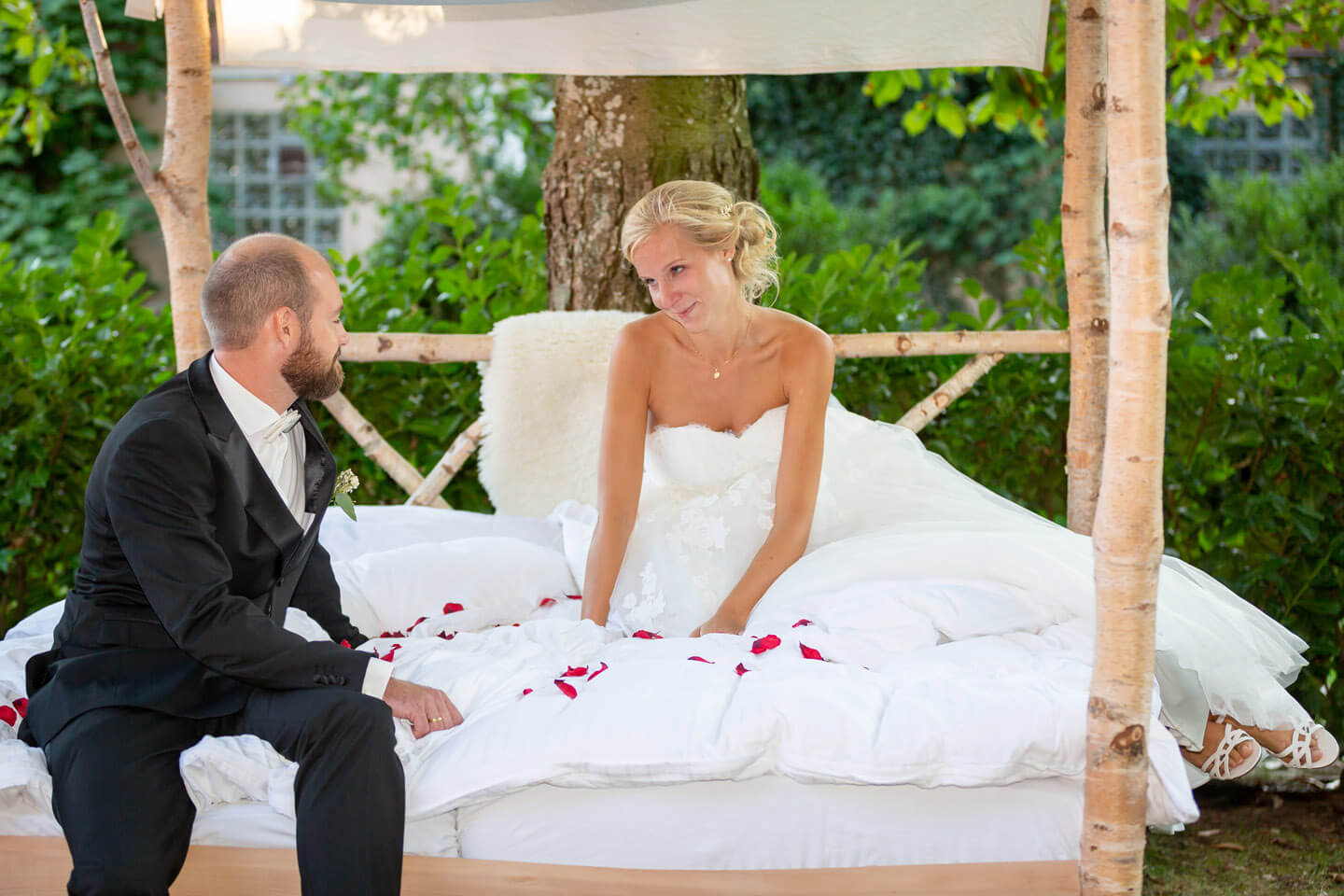 Hochzeitspaar im selbst gezimmerten Bett mit Rosenblättern