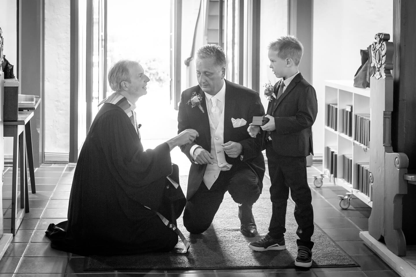 Pastor am Kircheneingang mit Braeutigam und Sohn