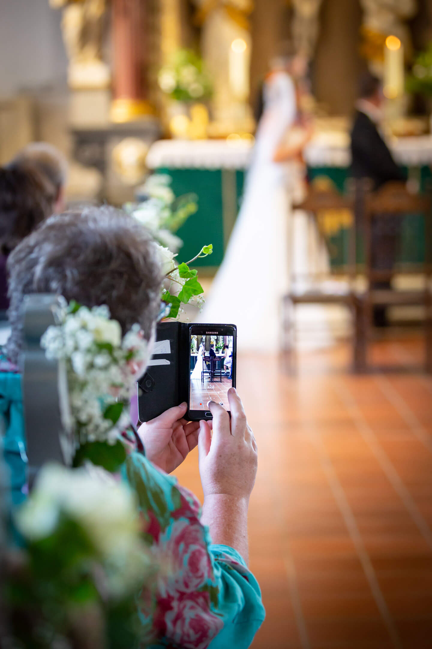 Kirchenbesucherin macht während der Trauung ein handyfoto vom Hochzeitspaar