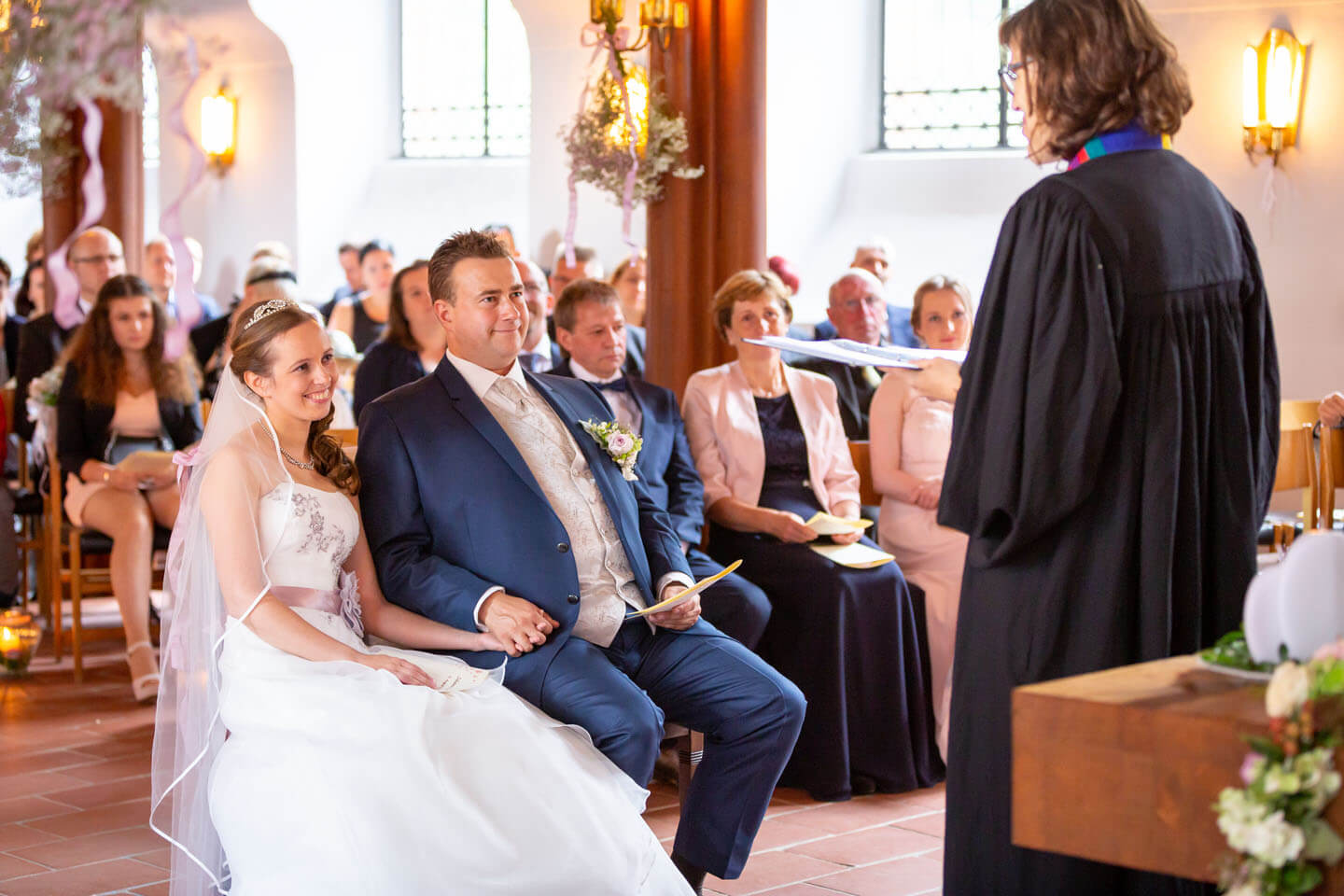 Hochzeitspaar blickt mit einem Lächeln die Pastorin in der St. Elisabeth-Kirche an