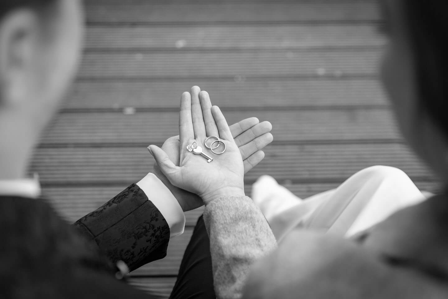 Brautpaar hält Trauringe und Schlüssel zum Liebesschloss