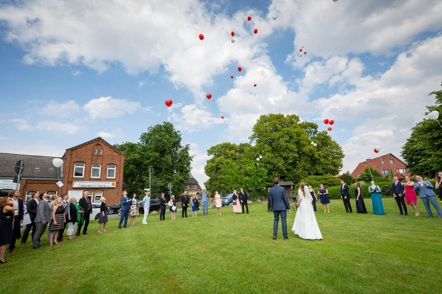 Hochzeitsgäste lassen rote Ballons in den Himmel steigen.