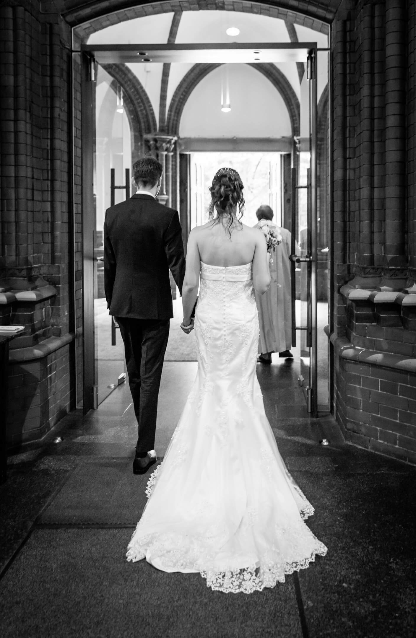 Brautpaar verlässt die Kirche. Das Brautkleid hat eine lange Schleppe.