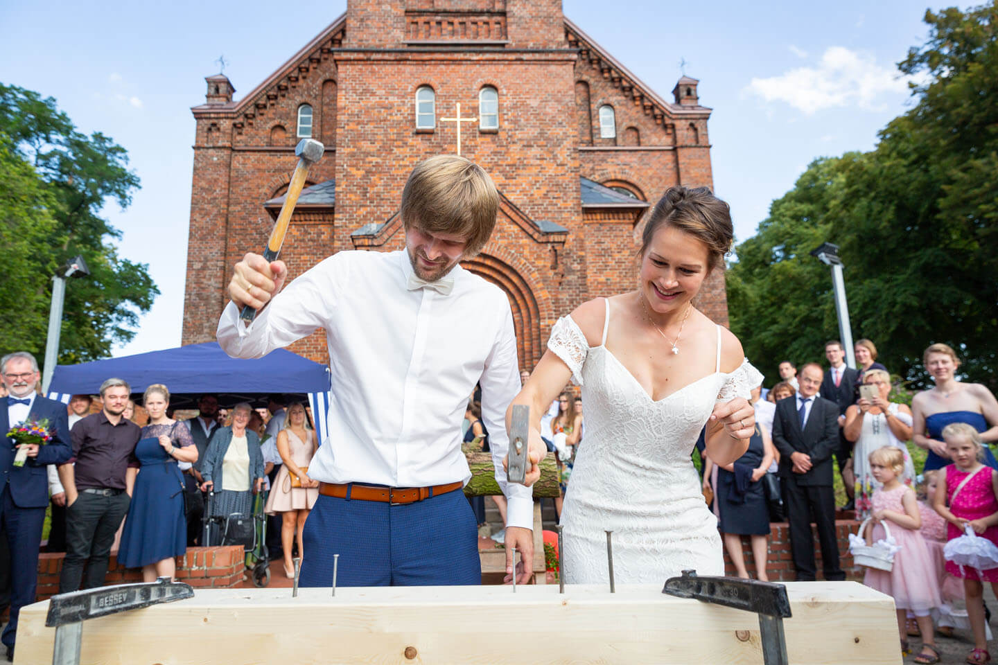 Brautpaar beim Hämmern vor der Kirche