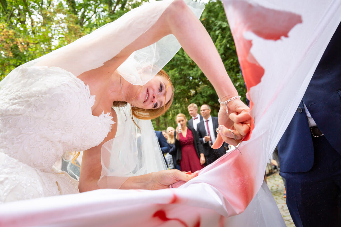 Braut schneidet mit Nagelschere Herz aus dem Bettlaken aus