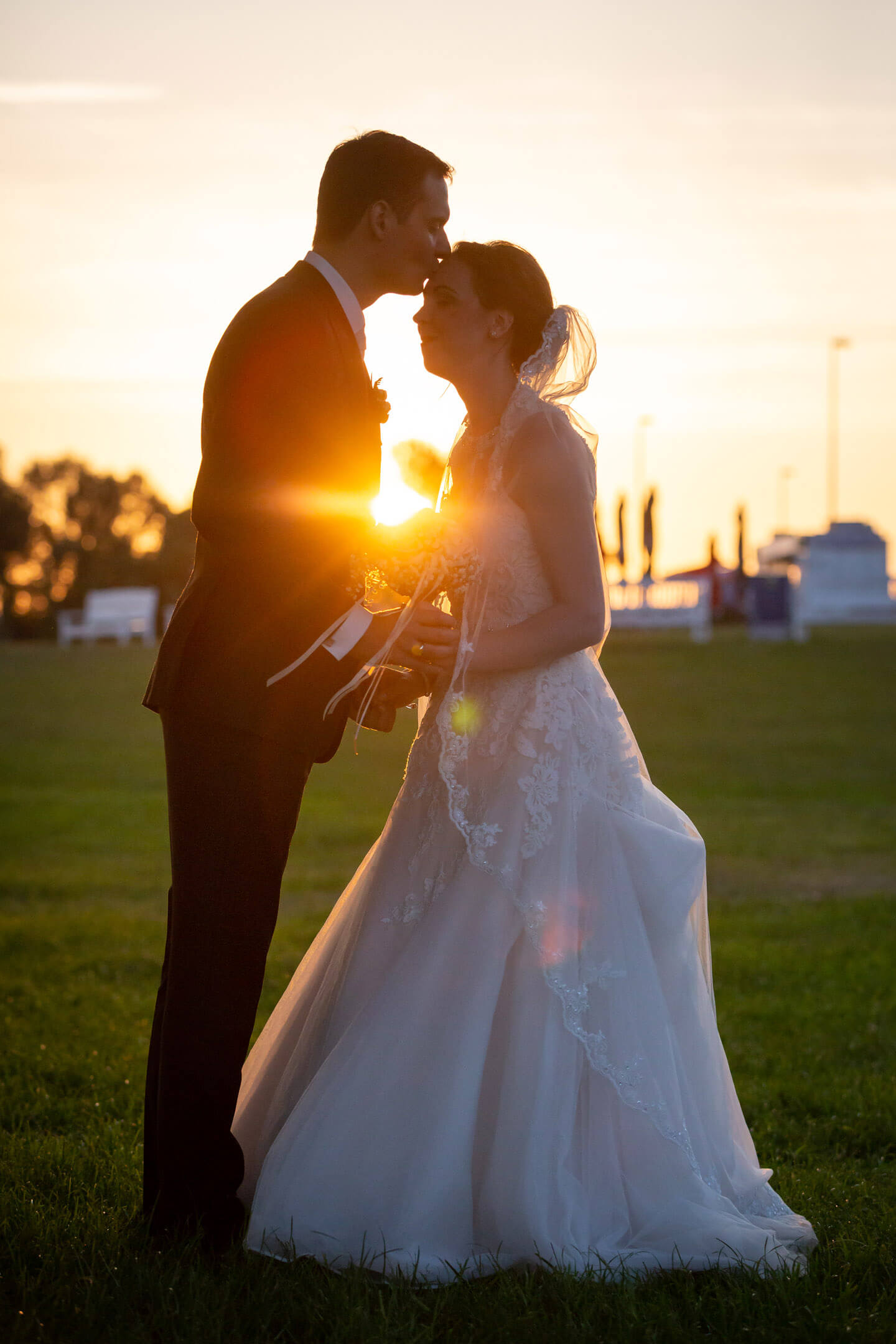Bräutigam küsst seiner Braut im Sonnenuntergang auf die Stirn.