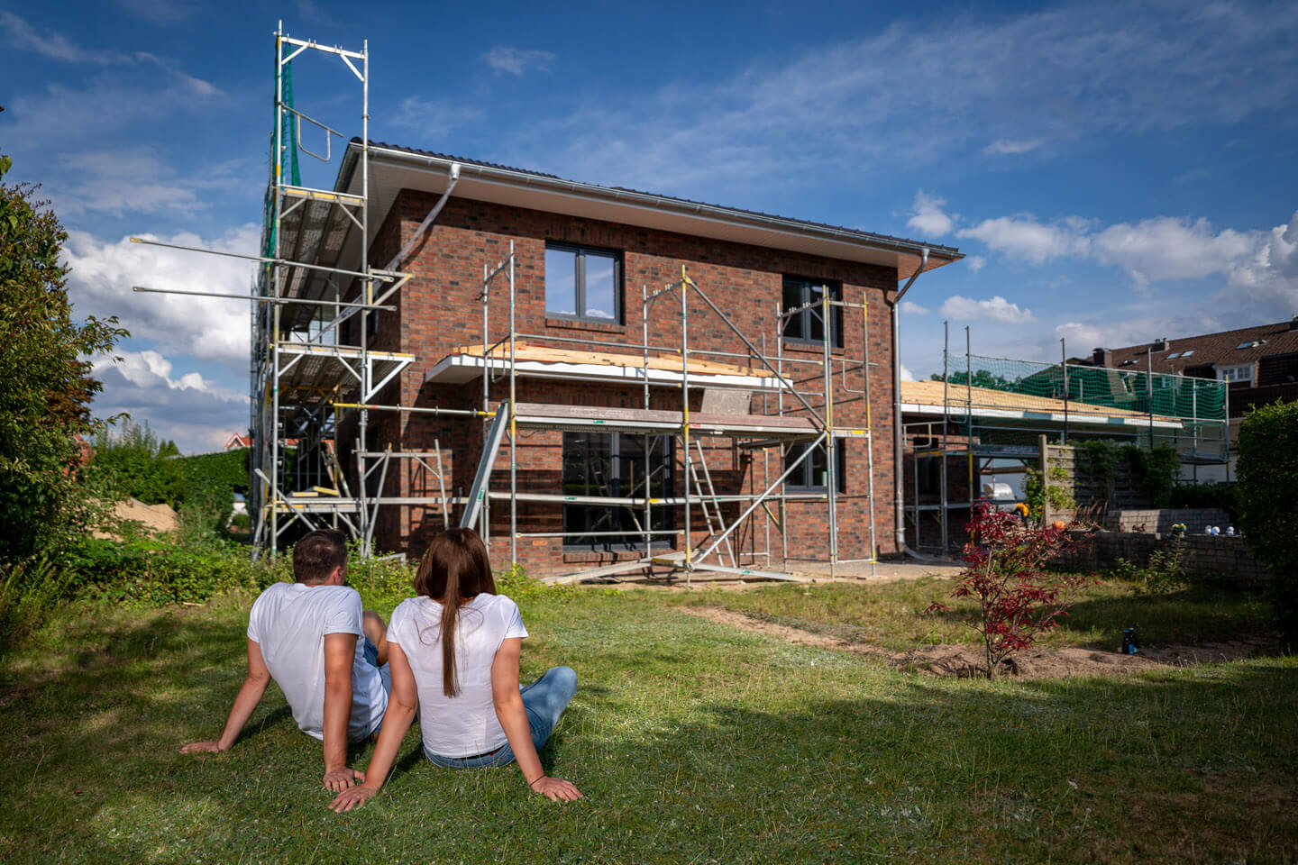 Junges Paar sitzt während eines Fotoshooting vor dem Rohbau ihrer Immobilie