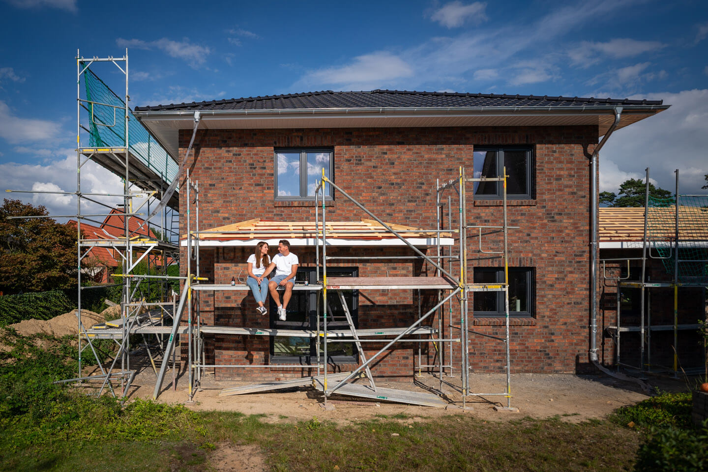 Verlobungspaar sitzt auf dem Baugerüst ihres Hauses