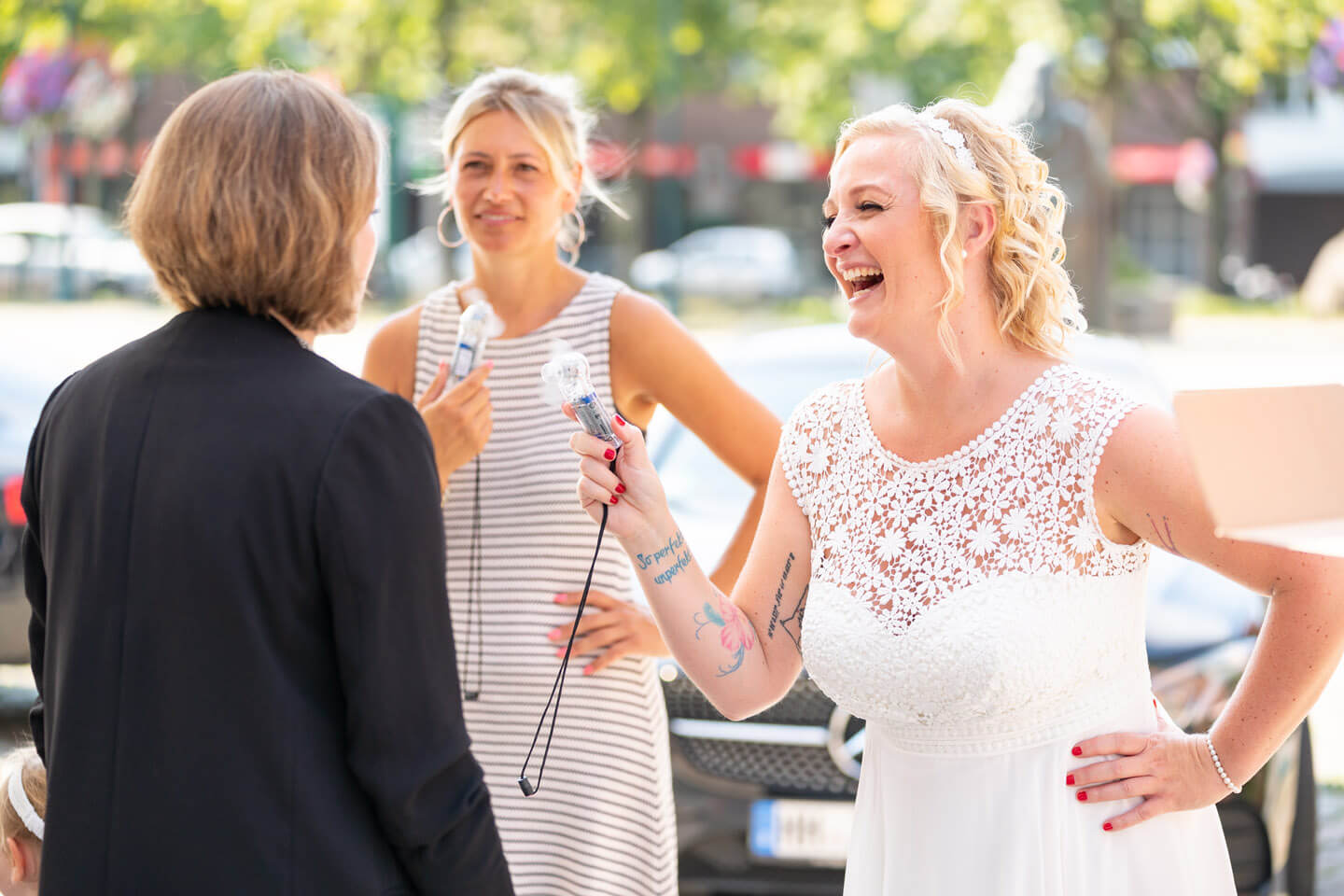 Braut mit Trauzeugin und Standesbeamtin mit Miniventilator an einem heißen Sommertag