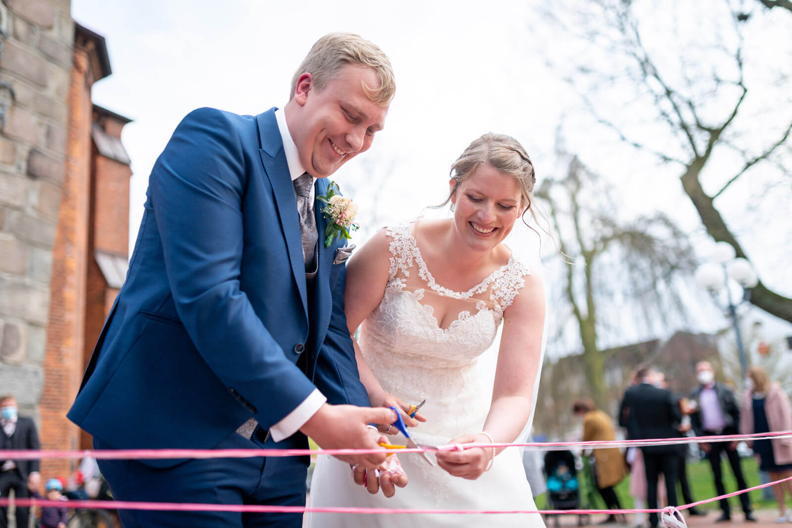 Brautpaar durchschneidet Bänder vor der Kirche