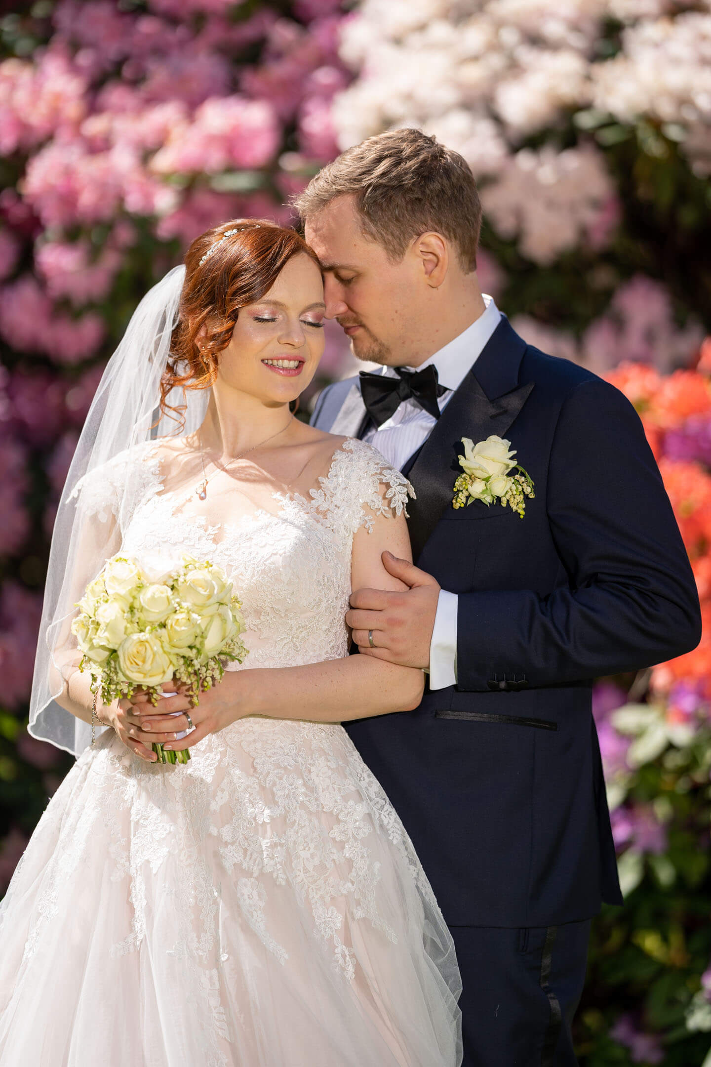 Klassisches Hochzeitsfoto vor blühendem Rhododendron.