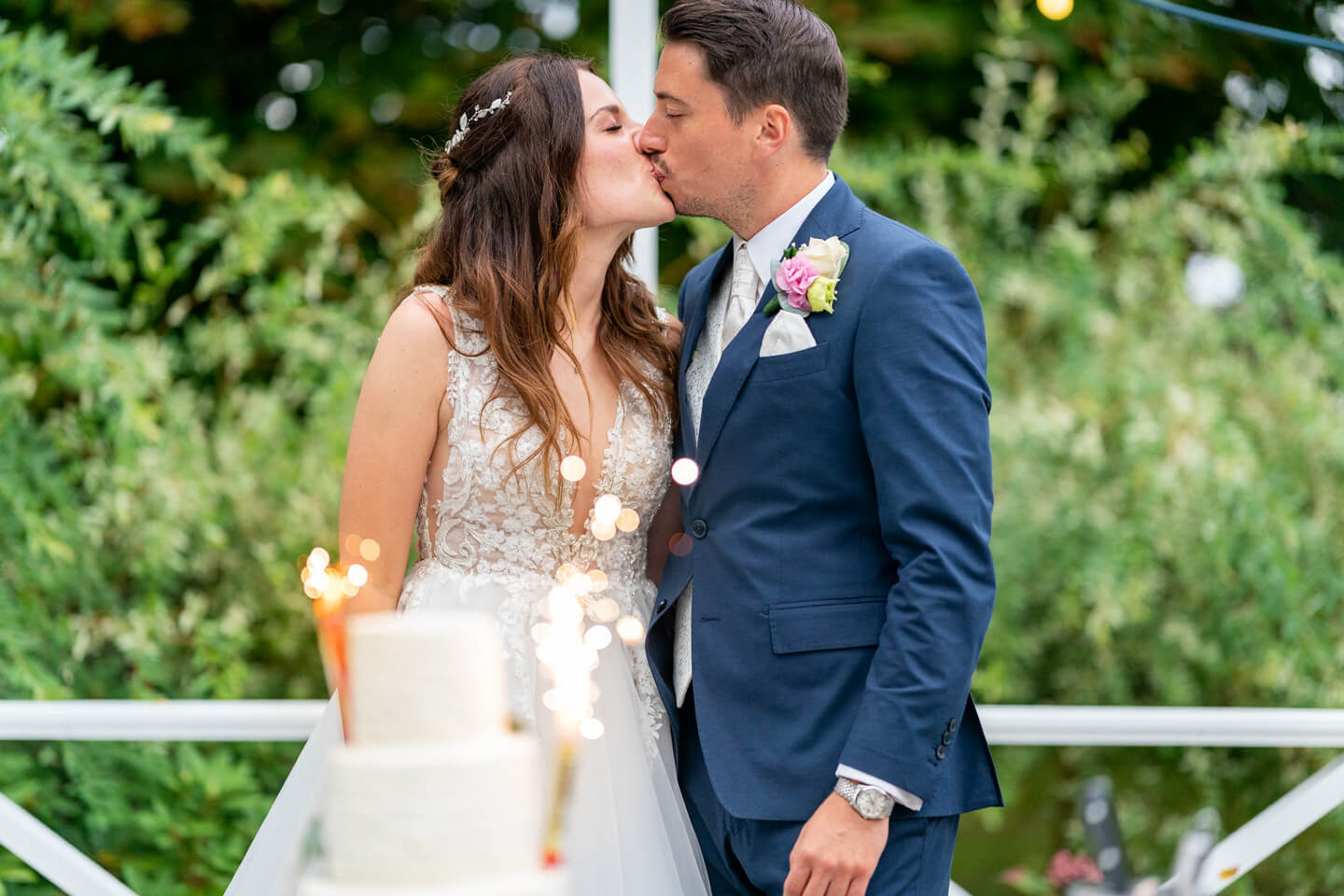 Brautpaar küsst sich vor der Hochzeitstorte.