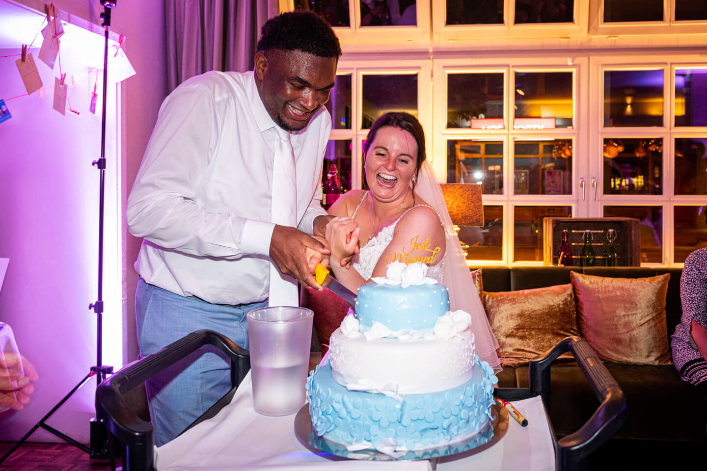 Brautpaar schneidet lachend die Hochzeitstorte an.